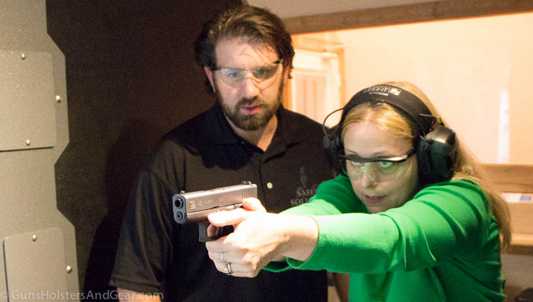 In this photo, Paul Carlson, a firearms trainer and deputy sheriff, trains a pretty blonde lady at an indoor shooting range. 