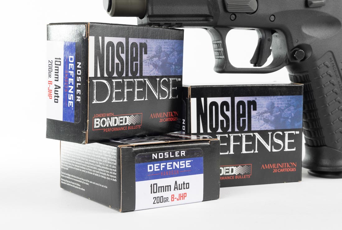 A close-up image of Nosler-branded 10mm Auto ammunition is displayed. The cartridges include both 180-grain jacketed hollow points and 200-grain defensive loads, which were used during the Springfield XD-M Elite OSP review. The brass cases are cleanly finished, and the hollow point bullets are designed for controlled expansion in defensive use. These rounds were tested alongside Blazer Brass practice ammo, confirming reliable feeding and cycling in the XD-M Elite. Chronograph data showed consistent velocity and energy, with groups under three inches at 15 yards. The photo emphasizes Nosler’s role as a premium ammunition choice for 10mm handguns. It illustrates the type of cartridges used during accuracy and reliability testing in the review.