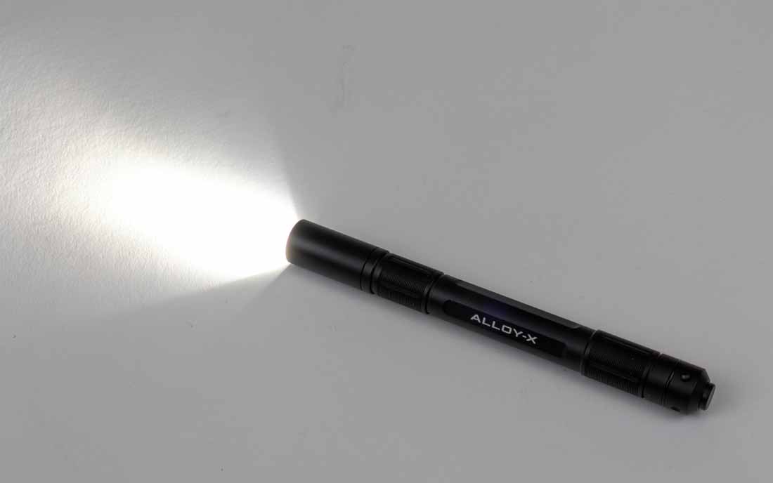 The Princeton Tec Alloy-X flashlight beam is shown illuminating a wall in a dimly lit environment. The beam has a broad central hotspot with smooth, even spill, giving it a flood-like quality despite being marketed as a spot beam. This makes it ideal for room searches, close-up work, and general everyday carry tasks. At maximum output, the beam delivers 400 lumens with a range of up to 56 meters. The light’s color temperature appears neutral white, providing clear visibility without excessive glare. This image illustrates how the Alloy-X balances brightness with a comfortable beam pattern for indoor and outdoor use. The wide spread ensures usable peripheral light while still providing a defined center for targeted illumination.