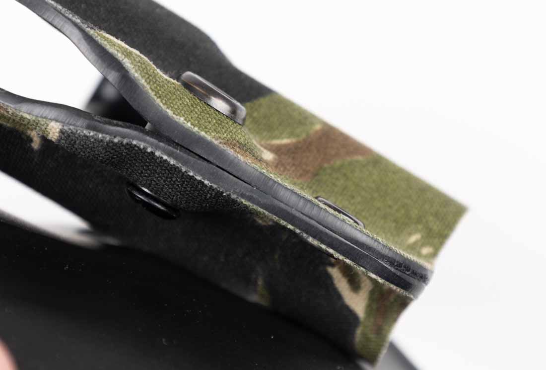 The image is a close-up of the edge of a Safariland Gravity holster, showing the layers of its construction. The innermost layer is SafariLaminate, a thermoformed material that maintains rigidity and shape even under heat exposure. Over this core, a Nylon Cordura wrap is applied, visible here as a textured fabric layer bonded to the outer surface. The image clearly shows the seam where the Cordura meets the laminate, illustrating the durability of the bond. This layered construction improves abrasion resistance while protecting the firearm’s finish from unnecessary wear. The close-up highlights the manufacturing quality and attention to detail in Safariland’s design. This view helps explain why the holster resists deformation, scuffing, and environmental wear in field conditions.