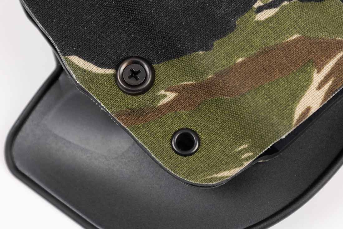 The image shows a close-up of the Safariland Gravity holster’s retention screw. The screw is positioned on the holster body near the trigger guard area, where it adjusts the clamping pressure of the molded SafariLaminate shell. Turning the screw increases or decreases the friction holding the pistol in place, allowing the user to customize draw resistance. This feature lets shooters balance speed and security for different carry situations. The adjustment point is recessed slightly to protect it from accidental movement during use. The surrounding area of the holster is finished in a Cordura wrap, with the screw set into a reinforced section. This design detail ensures long-term durability while giving users control over the holster’s retention feel.