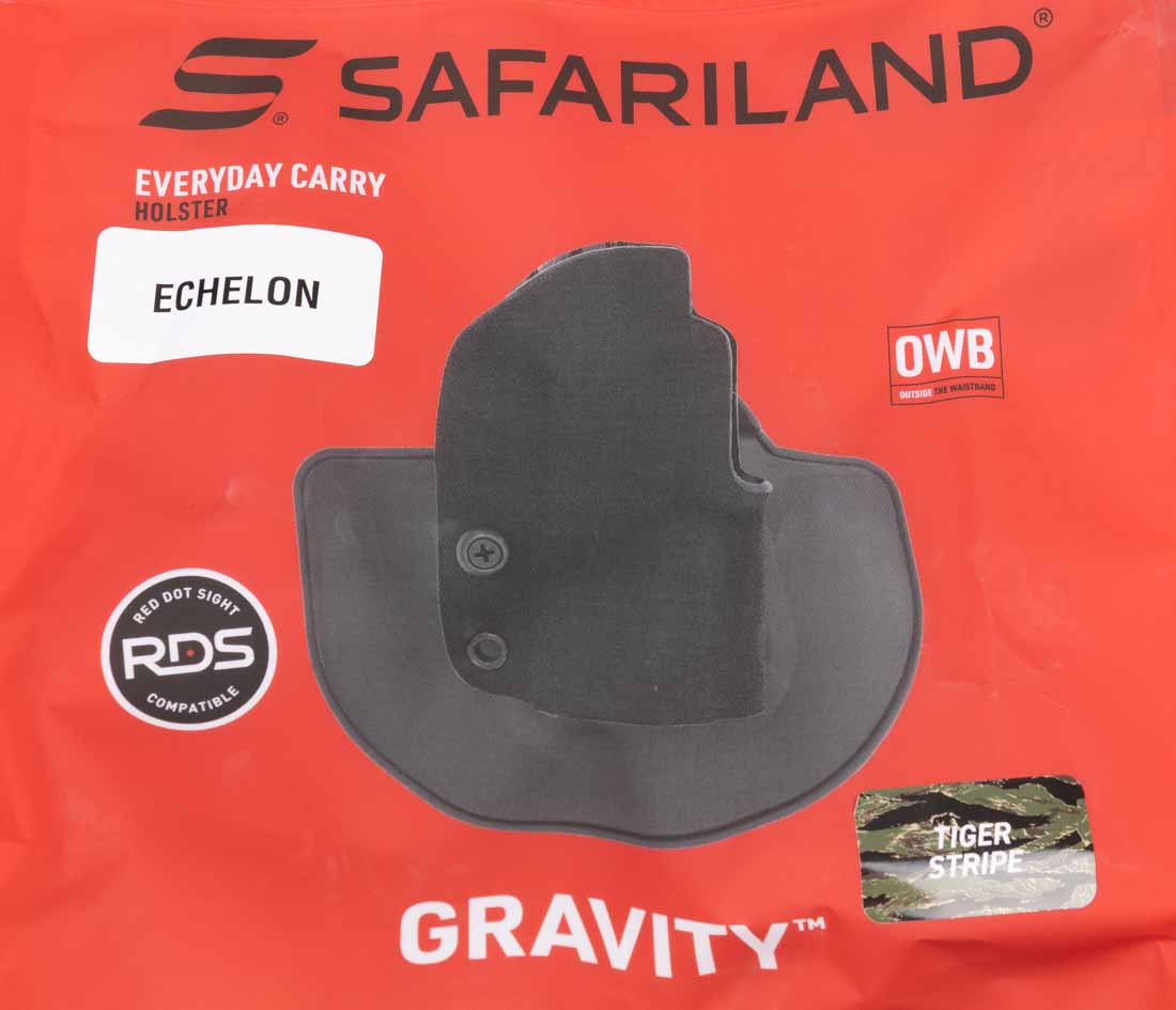 The image shows the retail packaging for a Safariland Gravity outside-the-waistband paddle holster. The holster is visible through a clear front panel, allowing the finish and overall shape to be seen without opening the package. Branding, product name, and key specifications are printed on the top and sides. The packaging lists the intended pistol fitment, retention style, and optic compatibility, making it easy for buyers to confirm they have the correct model. The holster is secured inside to prevent shifting during transport. The package design is straightforward, with emphasis on product visibility and essential information rather than excessive graphics. This ensures both retail display appeal and practical function for shipping or storage.