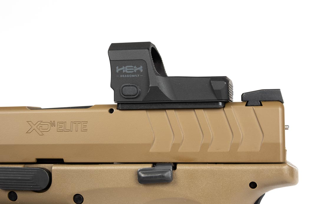 A Springfield Armory XD-M Elite OSP pistol chambered in 10mm Auto is pictured with a red dot sight mounted on its slide. The optic-ready design includes a factory-milled slide cut, making installation simple with just a screwdriver. The mounted optic co-witnesses with the pistol’s fiber optic front sight and tactical U-notch rear, ensuring a backup aiming option. The pistol retains its 4.5-inch match-grade barrel, striker-fired system, and ergonomic grip. The red dot enhances speed and precision, particularly for defensive use or competition shooting. This setup demonstrates the flexibility of the OSP platform, allowing shooters to choose between iron sights or optics. The image emphasizes the adaptability and modern design of the XD-M Elite 10mm handgun.