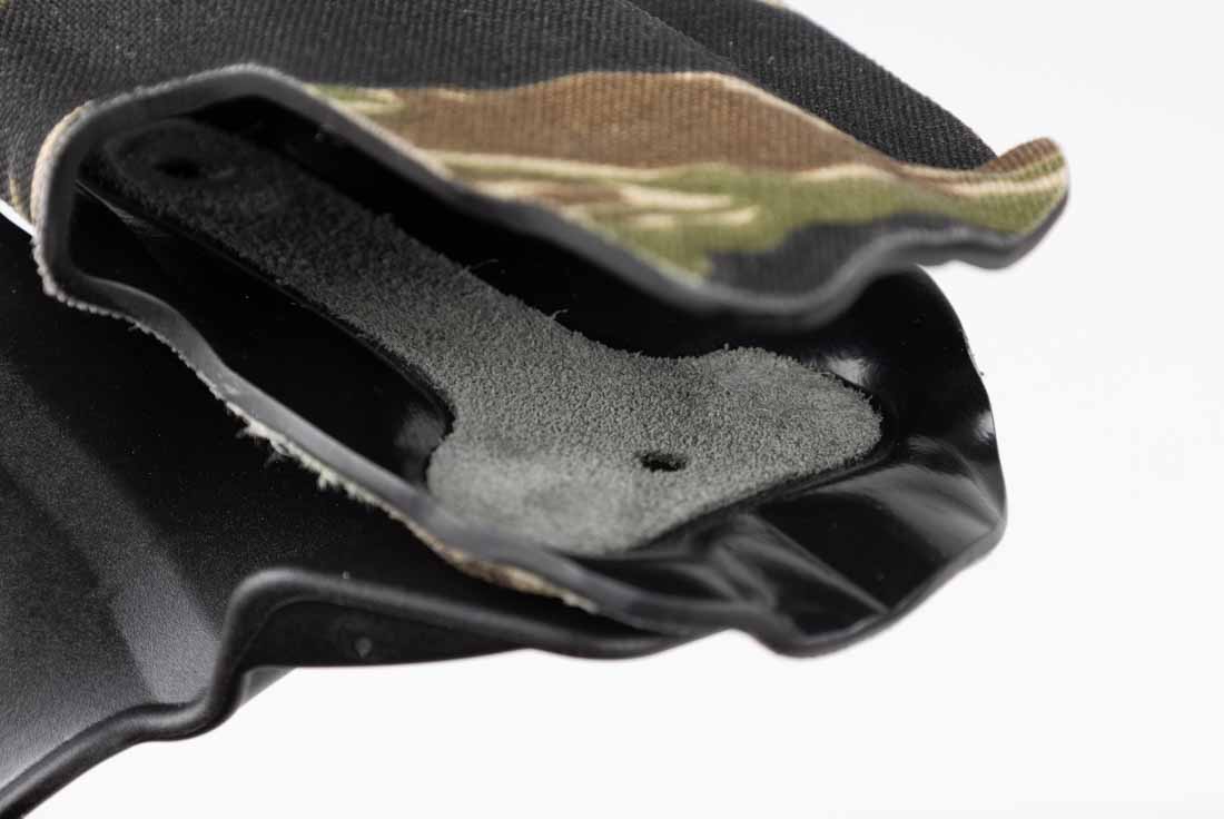 The image shows a close-up of the interior of the Safariland Gravity holster, revealing its suede lining. The lining is a soft, textured surface that covers the inside of the rigid SafariLaminate shell. This material reduces friction during the draw and reholster process, while also protecting the firearm’s finish from scratches and wear. The suede conforms closely to the holster’s molded shape, ensuring that retention remains consistent over time. This combination of a rigid exterior and a soft interior provides both stability and finish protection. The suede’s light color contrasts with the darker exterior wrap, making it visible in the close-up view. This interior detail highlights Safariland’s focus on functional durability and user firearm care.