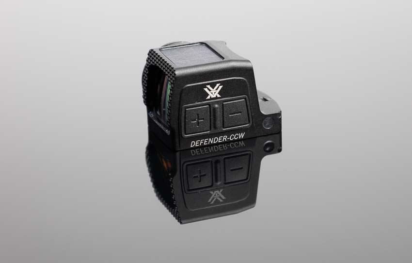 Vortex Defender-CCW Enclosed red dot sight displaying side-mounted brightness control buttons for manual dot intensity adjustment during shooting. The concealed carry pistol optic features accessible brightness controls allowing shooters to adjust red dot illumination without breaking firing grip. Defender-CCW brightness adjustment buttons provide intuitive up and down controls for optimizing dot visibility across lighting conditions. Enclosed red dot sights with side-mounted controls enable quick brightness changes during transitions from indoor to outdoor shooting environments. The manual brightness override on Vortex CCW enclosed optic works alongside auto-brightness feature for customized dot intensity. Pistol-mounted red dots for defensive carry require accessible controls the Defender-CCW delivers with ergonomic button placement. Duty-grade enclosed reflex sights incorporate user-friendly brightness adjustment without complicated menu systems or multiple button combinations. Concealed carry optics with side brightness controls allow dot intensity changes while maintaining proper shooting grip and sight alignment.