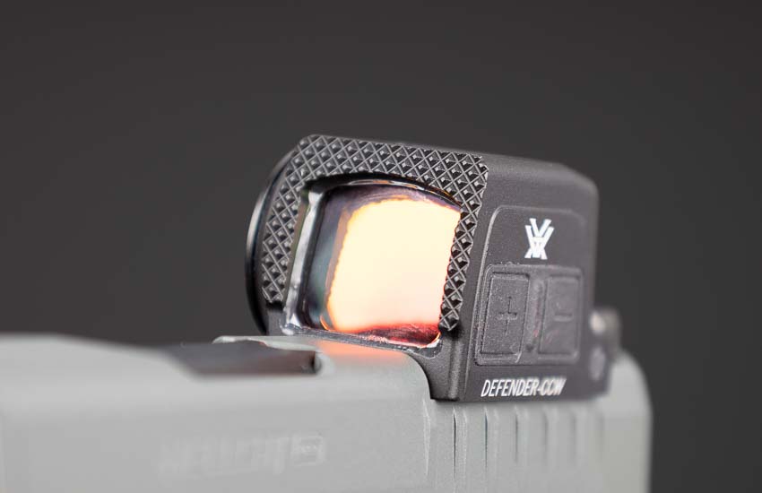 Vortex Defender-CCW Enclosed red dot sight showing front racking surface with aggressive serrations for emergency one-handed slide manipulation. The enclosed pistol optic features textured forward surface allowing shooters to rack slide against belt or hard surface during defensive scenarios. Defender-CCW emergency racking serrations provide crucial capability when support hand is injured or compromised during self-defense situations. Concealed carry red dot sights with functional racking surfaces deliver practical defensive features beyond basic target acquisition. The front serrations on Vortex CCW enclosed optic enable one-handed malfunction clearance and chamber checks during carry. Pistol-mounted red dots for EDC applications benefit from emergency slide manipulation capabilities the Defender-CCW provides. Duty-grade enclosed reflex sights incorporate practical defensive features like racking surfaces for real-world concealed carry needs. Micro pistol optics with forward serrations allow emergency slide operation when normal two-handed manipulation isn't possible.
