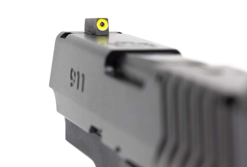 An extreme close-up of the Springfield 911's Pro-Glo front sight reveals the green tritium vial surrounded by a yellow photoluminescent ring designed for rapid target acquisition in variable lighting. The Springfield 911 9mm review highlights front sight visibility as a key defensive feature. Tritium front sights glow continuously for twenty-four-hour aiming capability. The Springfield Armory 911 combines tritium and photoluminescent technologies for maximum visibility. Bright front sights enable faster shot placement during high-stress encounters. Quality night sights improve low-light shooting performance significantly.