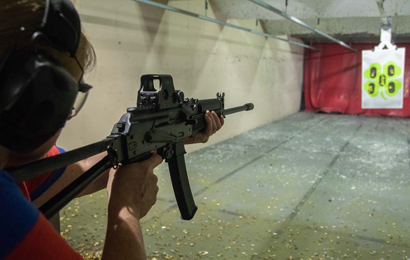 A blonde woman aims and fires the Kalashnikov KR-9 rifle at an indoor shooting range facility. The Kalashnikov KR-9 suits shooters of varying experience levels. Pistol caliber carbines produce manageable recoil for all users. The KUSA 9mm pistol caliber carbine offers intuitive operation for beginners. Blowback-operated firearms deliver gentle shooting characteristics. AK-pattern carbines accommodate diverse shooter body types effectively.