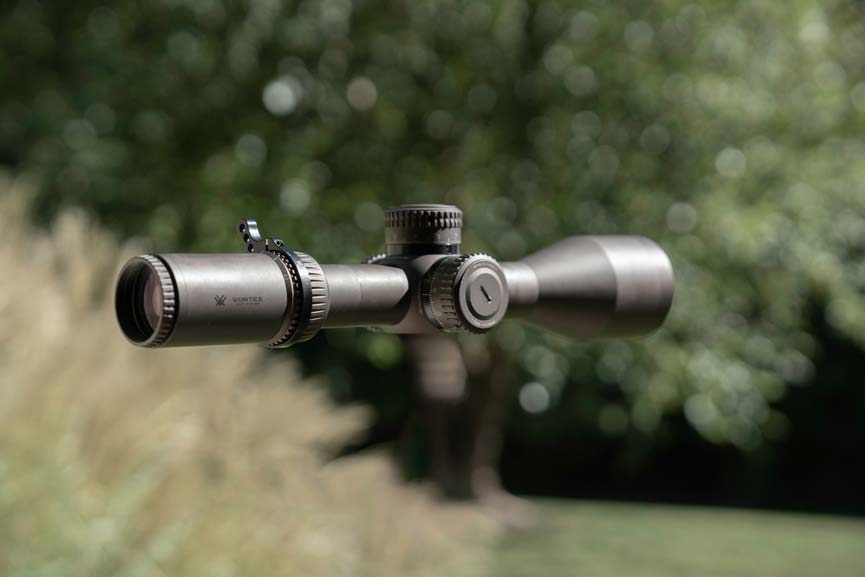 a close-up of a rifle scope against a blurred green outdoor background