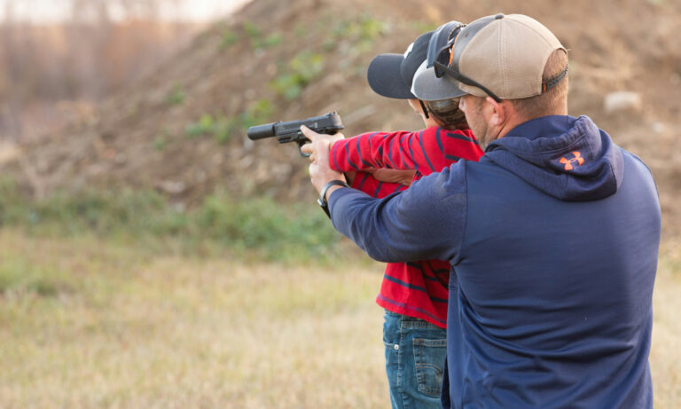 a man helping a woman aim a pistol with a silencer at an outdoor range
